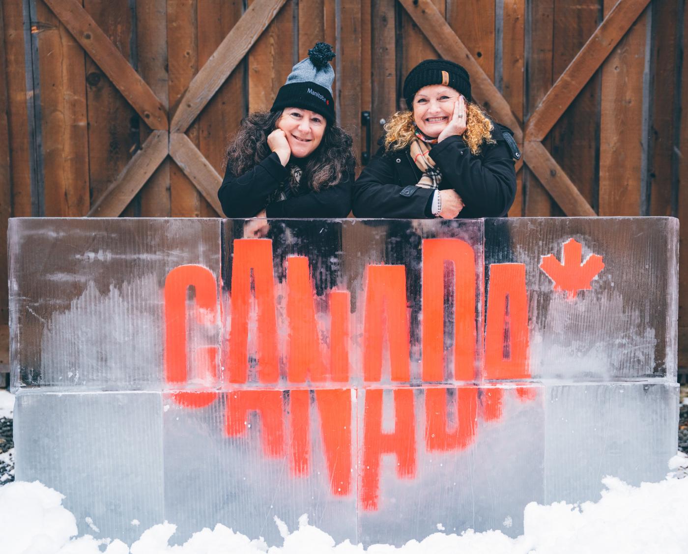 Two women pose behind an ice counter with a red Canada logo in the middle of it.