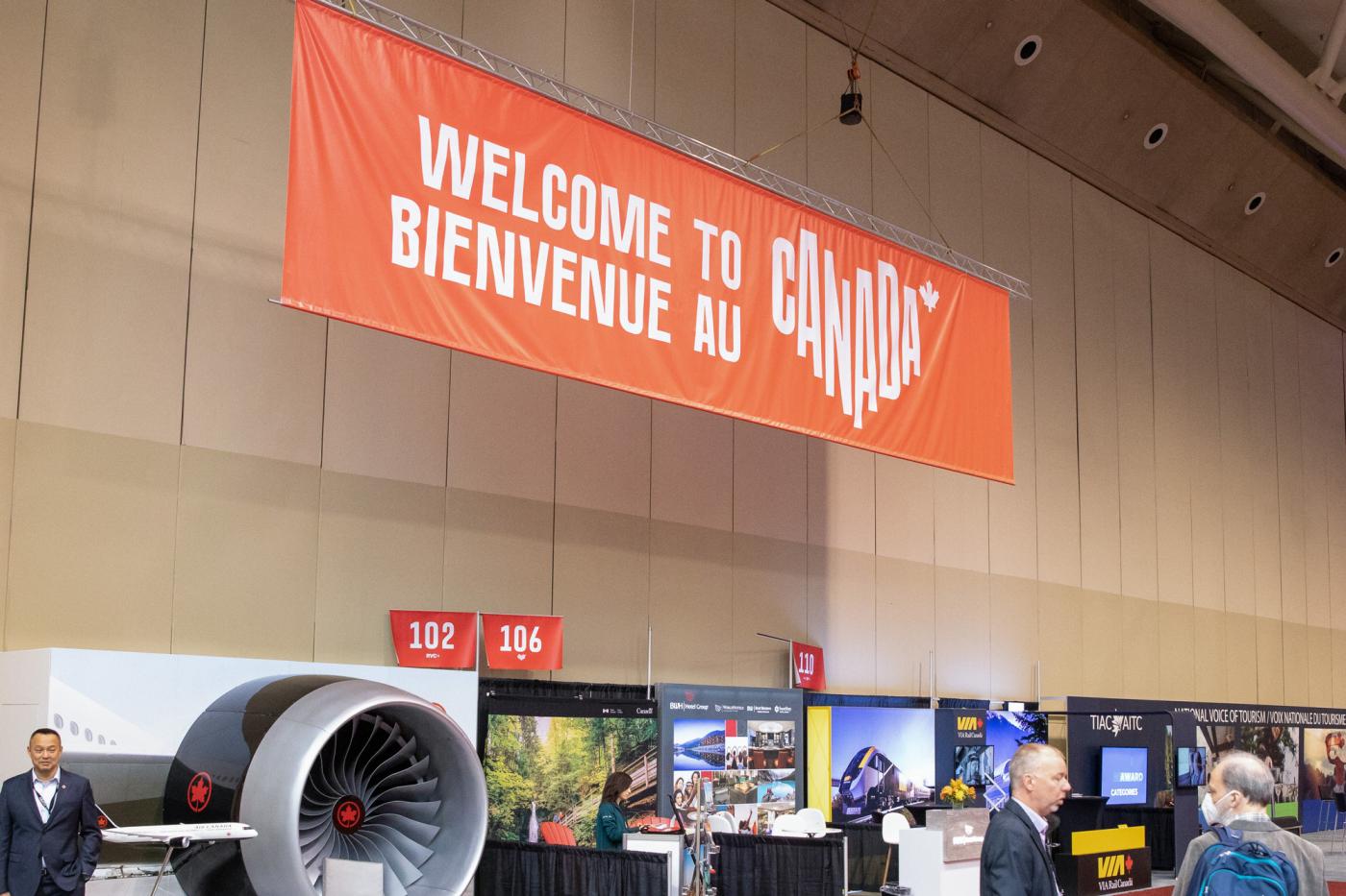 A large red banner hangs in a convention space that says "Welcome to/ Bienvenue au Canada"