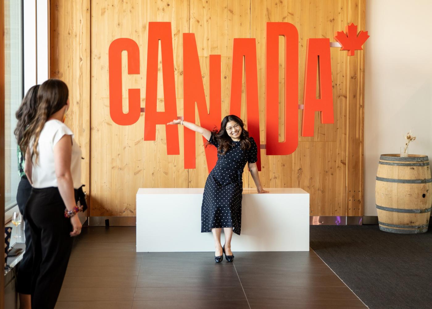 A woman poses in front of a large 3D version of the Canada logo