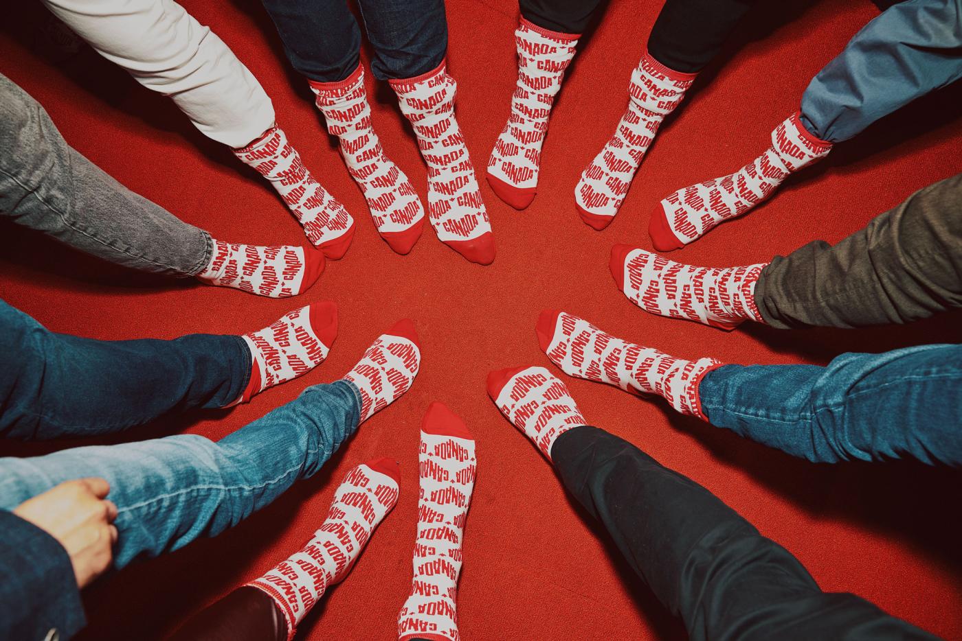 A group of people wearing red and white Canada branded socks are stepping together to make a circle.
