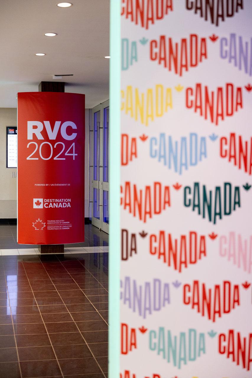 Un couloir avec un panneau rouge sur lequel il est écrit « RVC 2024 ». À côté, il y a un mur coloré décoré de plusieurs logos Canada.