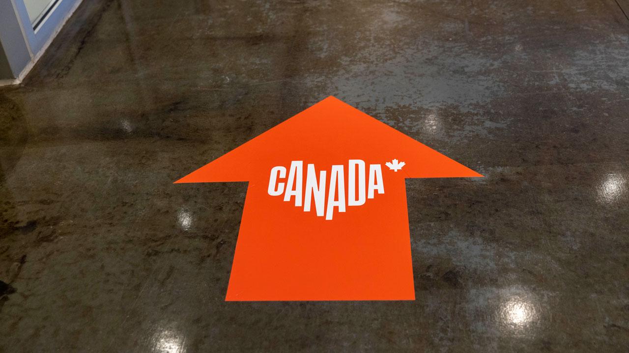 An arrow on the ground pointing forward with the Destination Canada logo